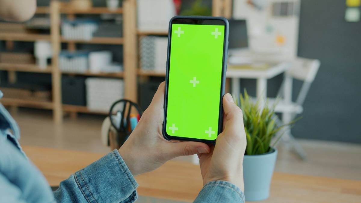 Close-up of female hands holding chroma key green screen smartphone in office. Modern technology, media content and contemporary gadgets concept.